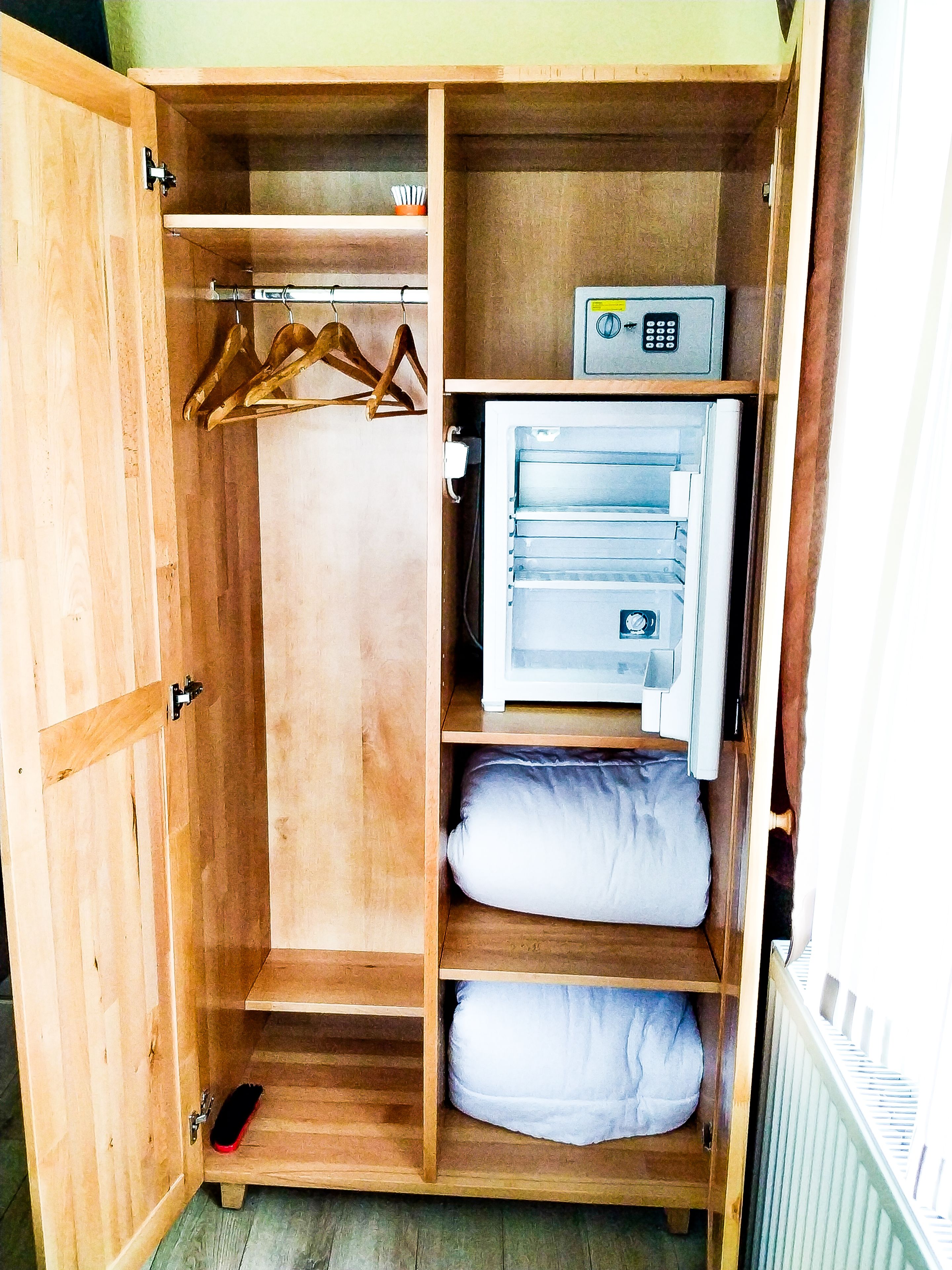 A wooden wardrobe with multiple shelves, a hanging rod, and a built-in mini-fridge.