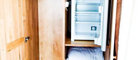 A wooden wardrobe with multiple shelves, a hanging rod, and a built-in mini-fridge.
