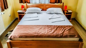 A neatly made bed with pillows, a wooden headboard, two bedside tables with lamps, and a window with curtains. - Venesis House (Sighisoara)