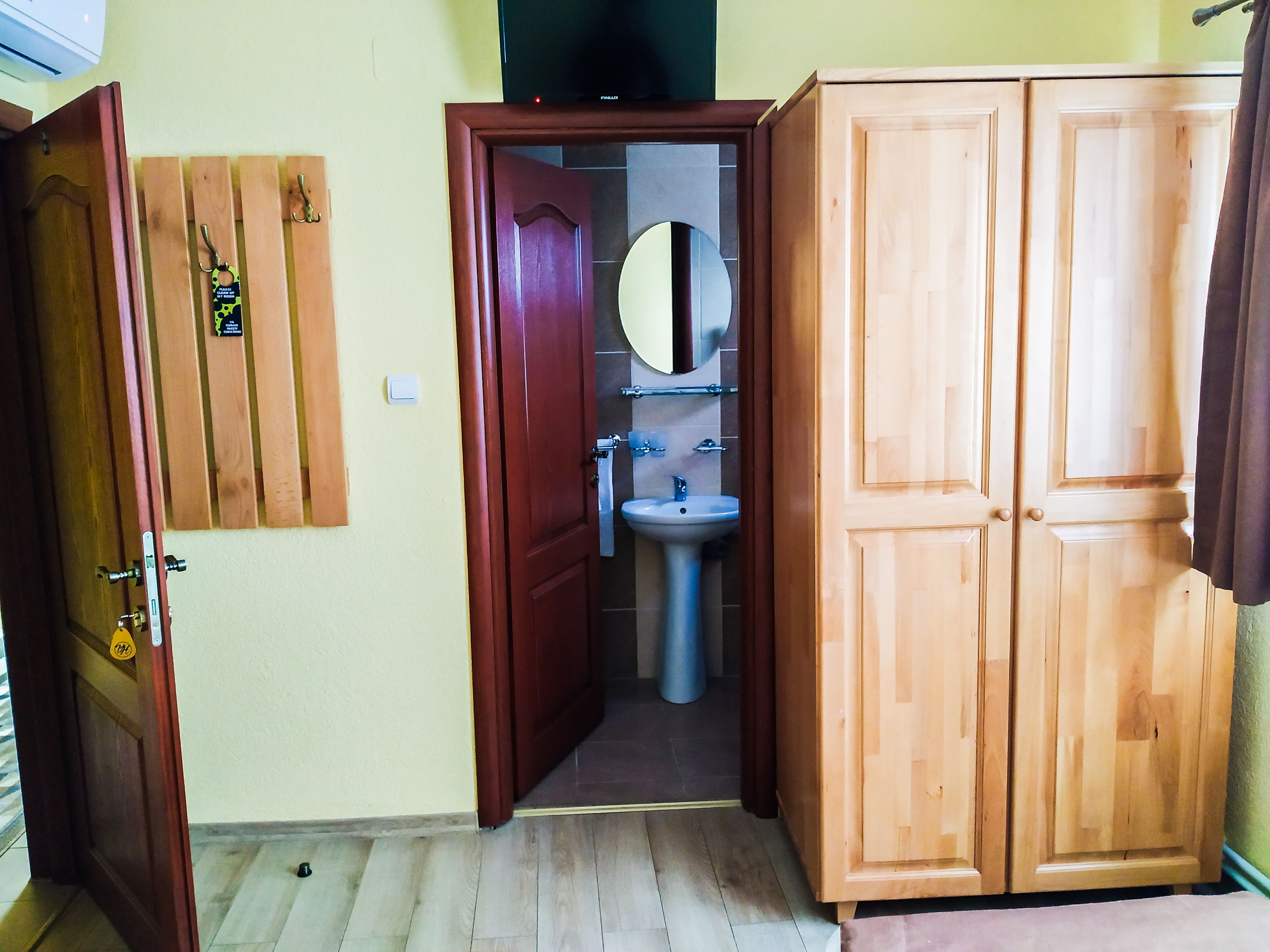 Una habitación con un armario de madera, un baño con lavamanos y espejo, y una puerta con cerradura.