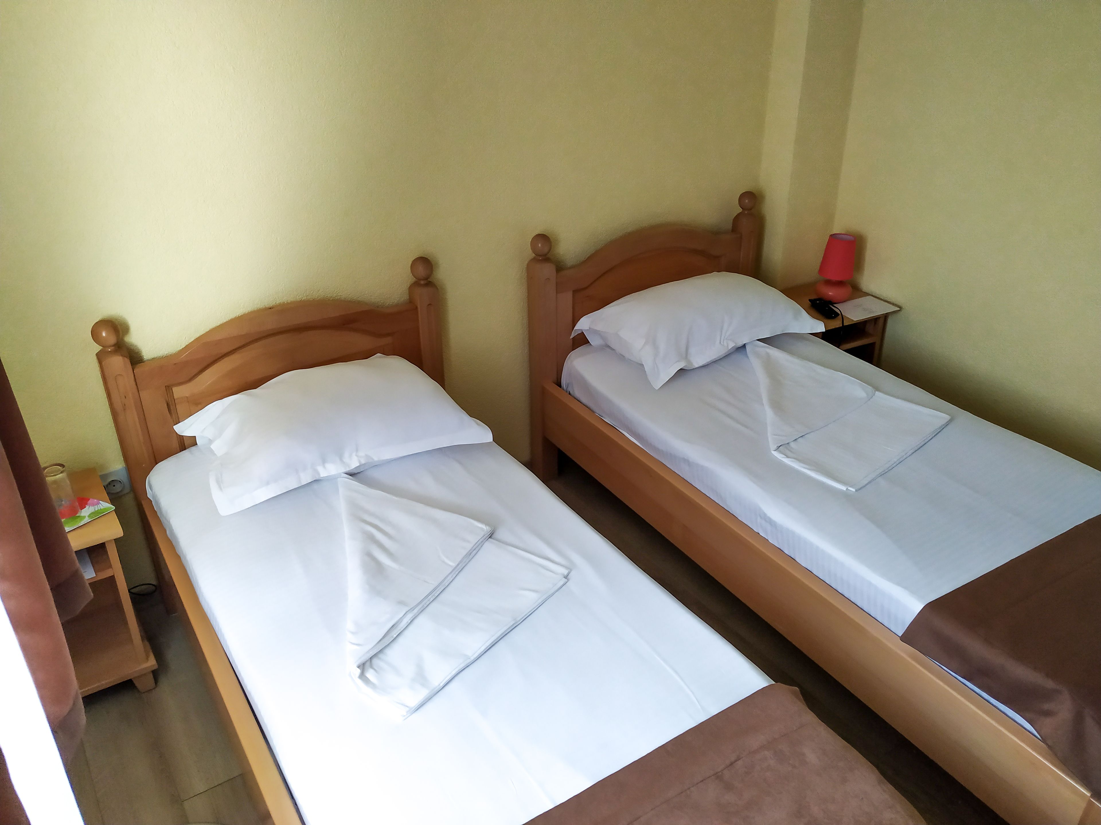 Two single beds with wooden headboards, white linens, and a small bedside table with a red object on it.