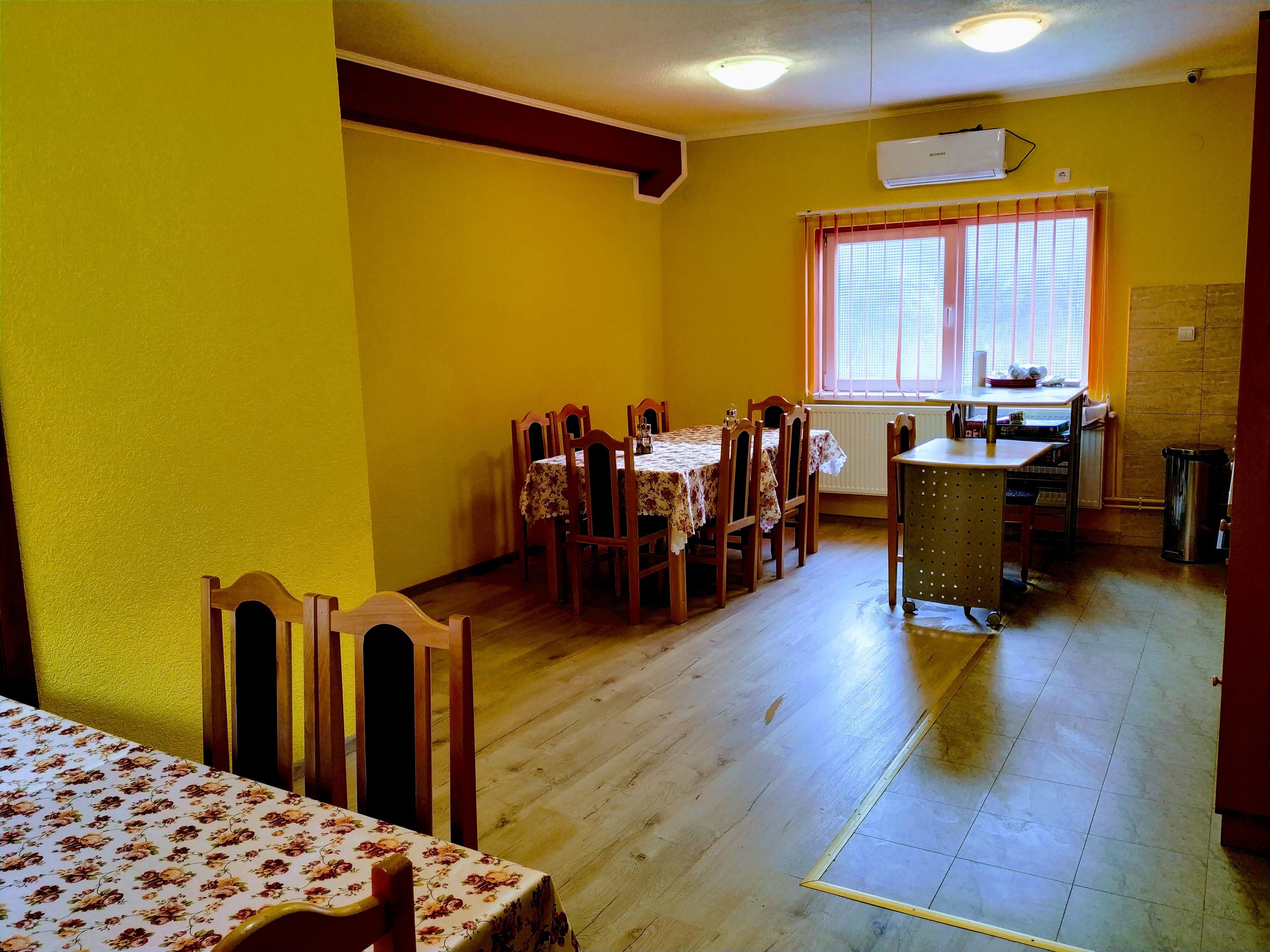 A dining area with wooden chairs and a table, a window with blinds, and a radiator.