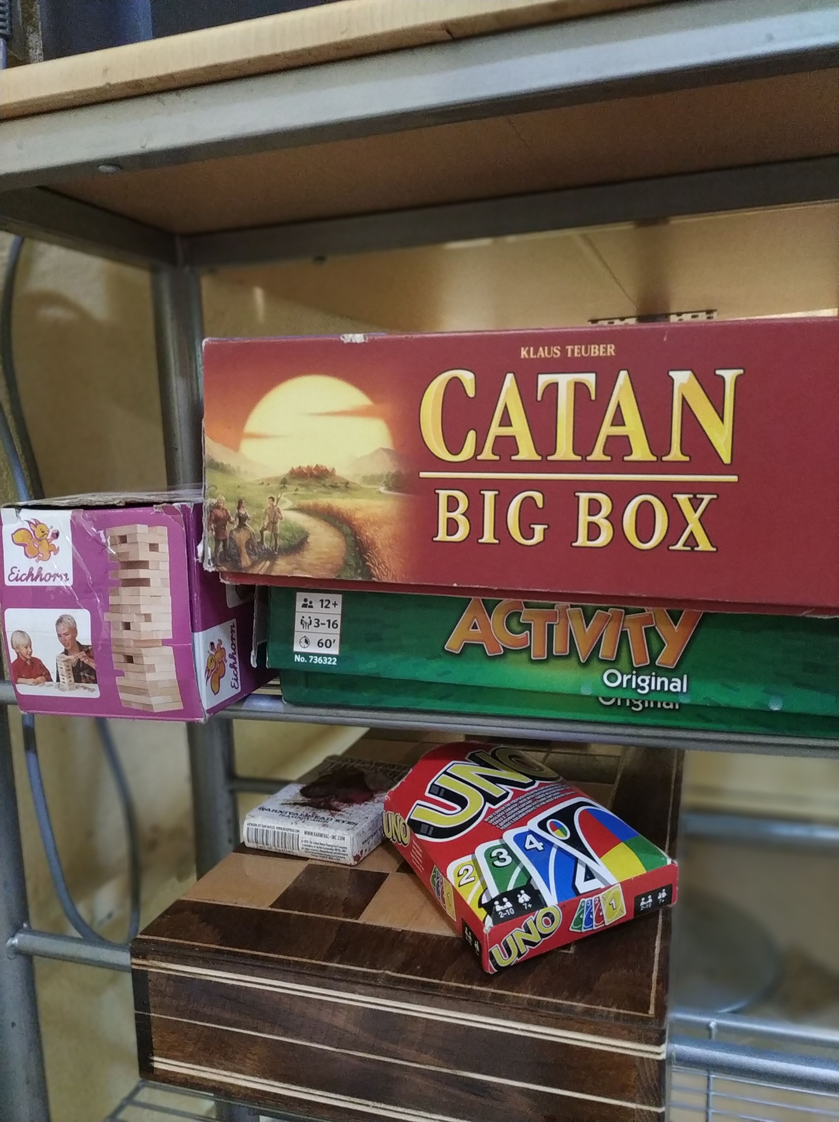 Ein Regal mit einem Catan Big-Box-Spiel, einem Jenga-Turm und einem Monopoly-Spiel.