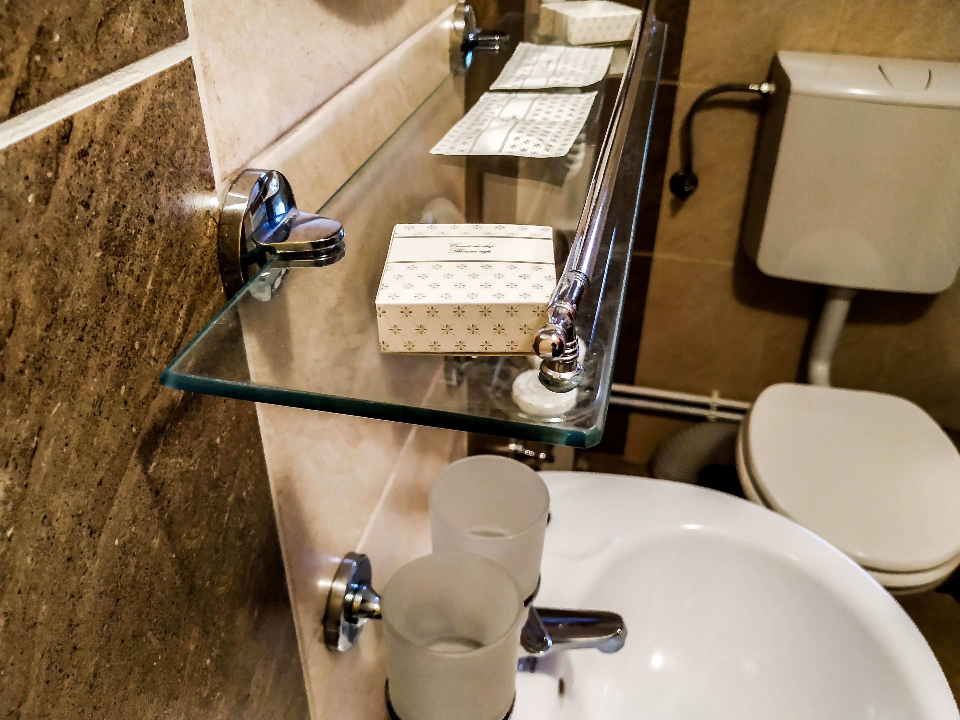 A bathroom with a glass shelf holding toiletries, a white sink, and a toilet.