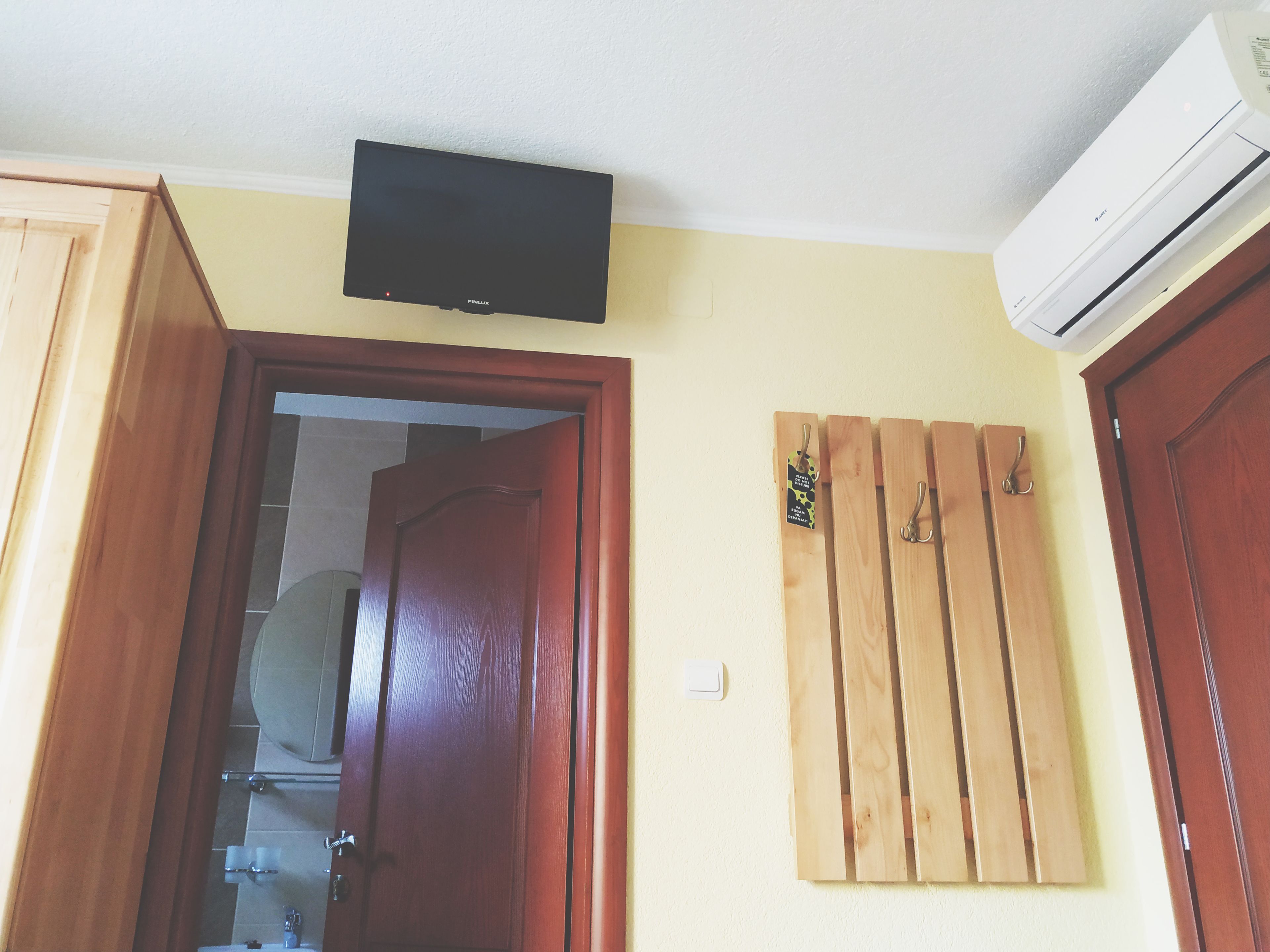 Una habitación con una puerta de madera, un televisor montado y un equipo de aire acondicionado instalado en la pared.