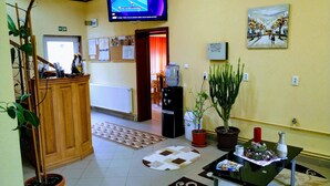 A reception area with a wooden desk, a television mounted on the wall, potted plants, and a painting. - Venesis House (Sighisoara)