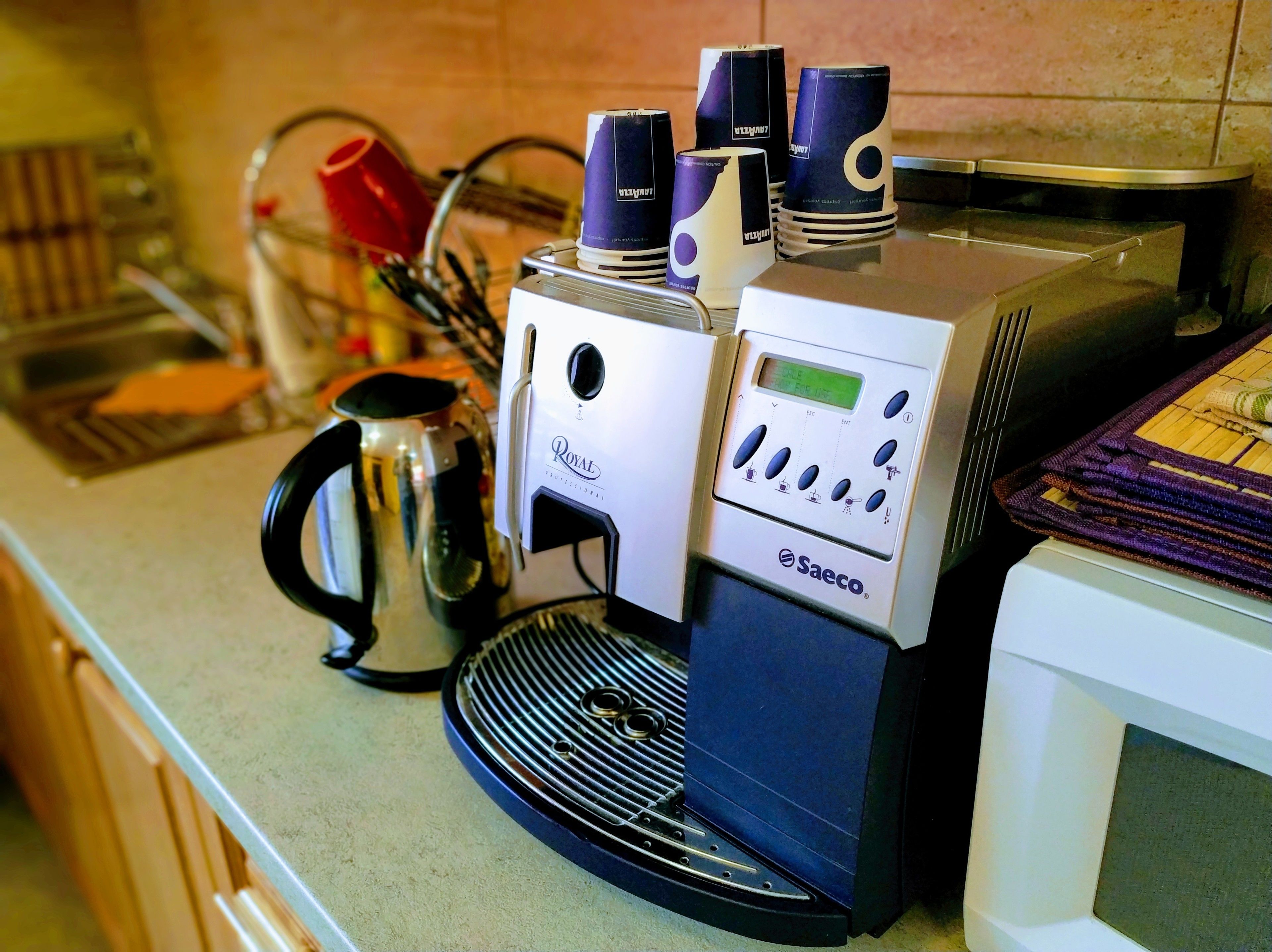 Una cafetera con pantalla digital y botones, una tetera y un microondas sobre una encimera de cocina.