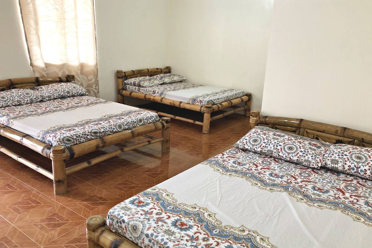 A room with three wooden beds with patterned bedding, a tiled floor, and a window with curtains.
