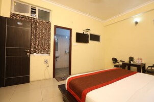 Habitación de hotel con cama, escritorio, silla, televisor y baño visible a través de una puerta.