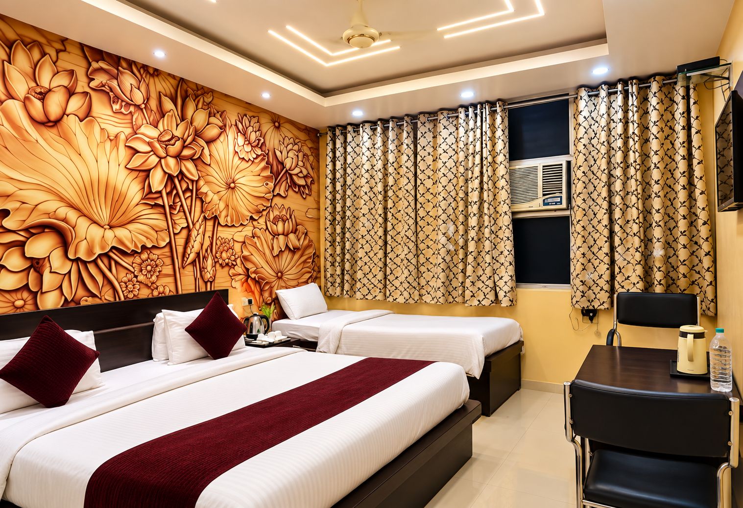 A hotel room with two beds, a large floral mural, patterned curtains, a desk with a chair, and a flat-screen TV.