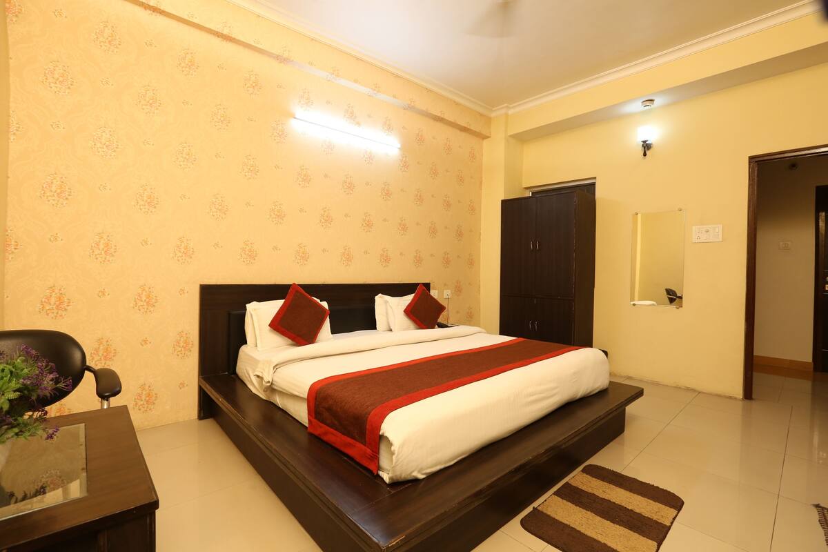A hotel room with a large bed, a desk, and a chair. There is a mirror on the wall and a door leading to another room.