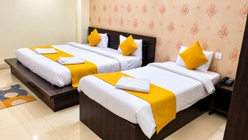 Dos camas individuales con ropa de cama blanca y detalles en amarillo, un cabecero de madera y un teléfono en la mesita de noche.