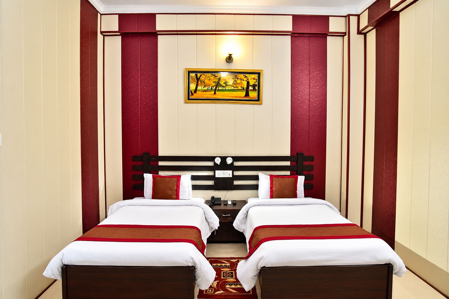 A hotel room with two beds, a red and white color scheme, a painting on the wall, and a nightstand between the beds.