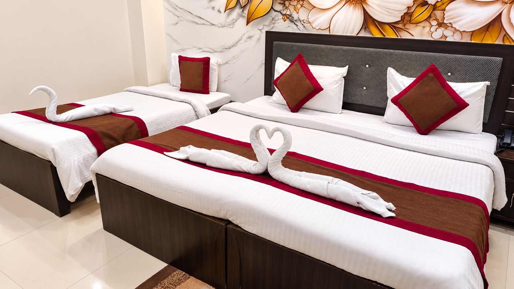 A hotel room with two beds, each with a swan-shaped towel and red accents.