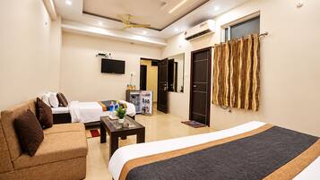Quarto de hotel com cama, sofá, mesa de centro, televisão e guarda-roupa.