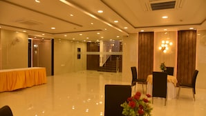 A spacious hotel lobby with a polished floor, a reception area, a staircase, and a dining area with chairs and a table. - Hotel Nexus (Lucknow)