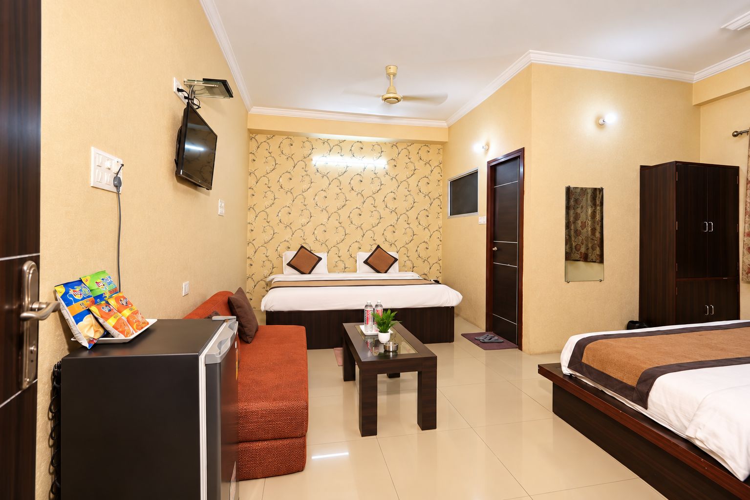 A hotel room with a bed, a sofa, a small table, a TV, and a wardrobe.