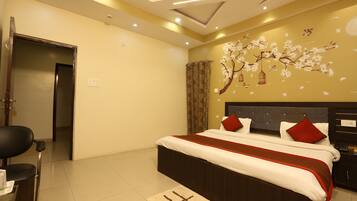 A hotel room with a bed, a desk, and a chair. There is a window with curtains and a wall with a floral mural.