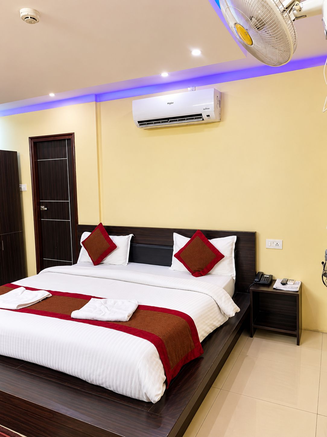 A hotel room with a bed, bedside table, and an air conditioning unit.