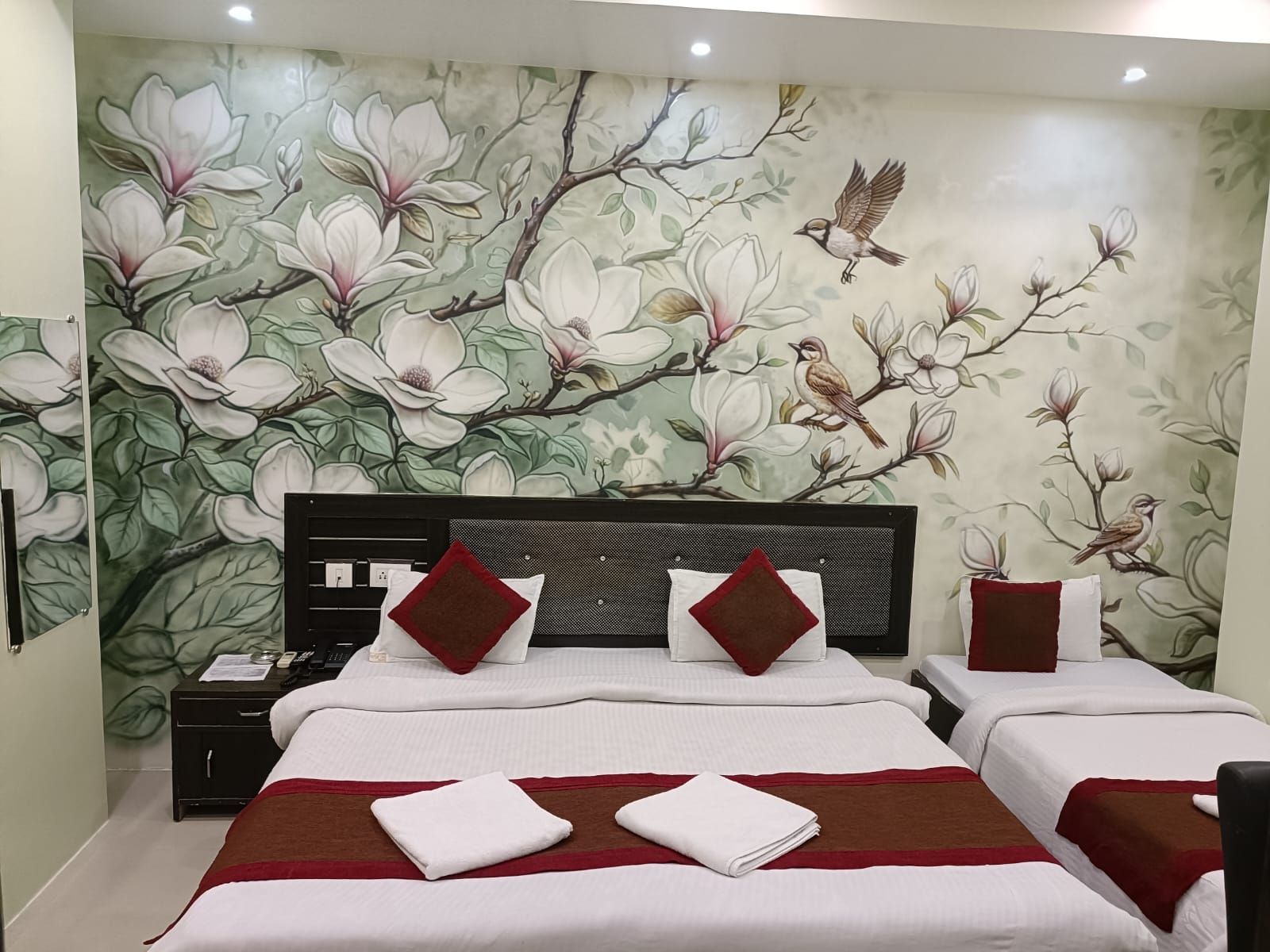A hotel room with two beds, a nightstand, and a wall mural of flowers and birds.