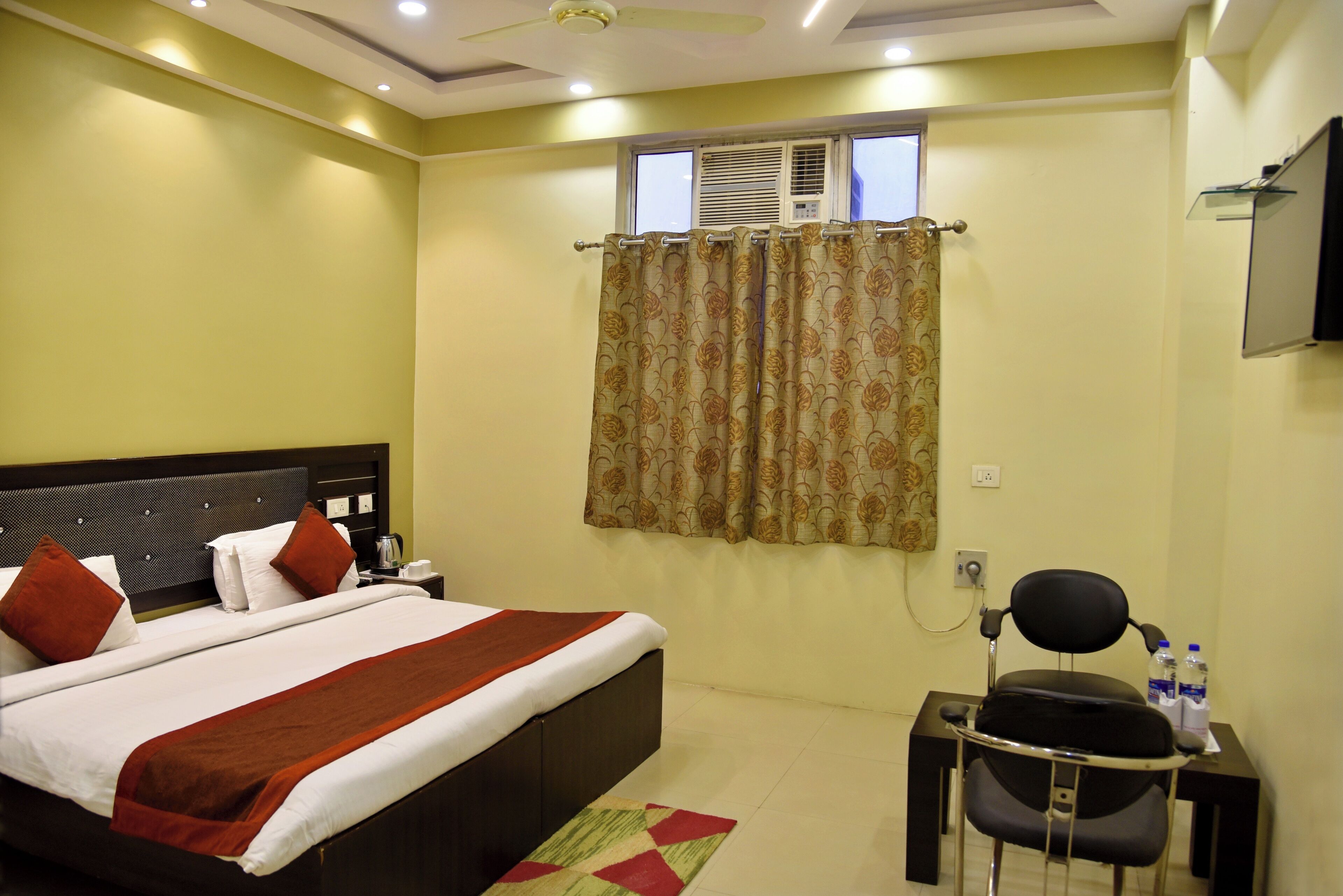 A bedroom with a bed, a desk, a chair, a window with curtains, and a ceiling fan.