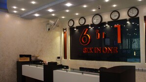 A reception area with a glass counter, multiple clocks, and a sign reading "6 in 1 Six in One". - Six In One (Malé)