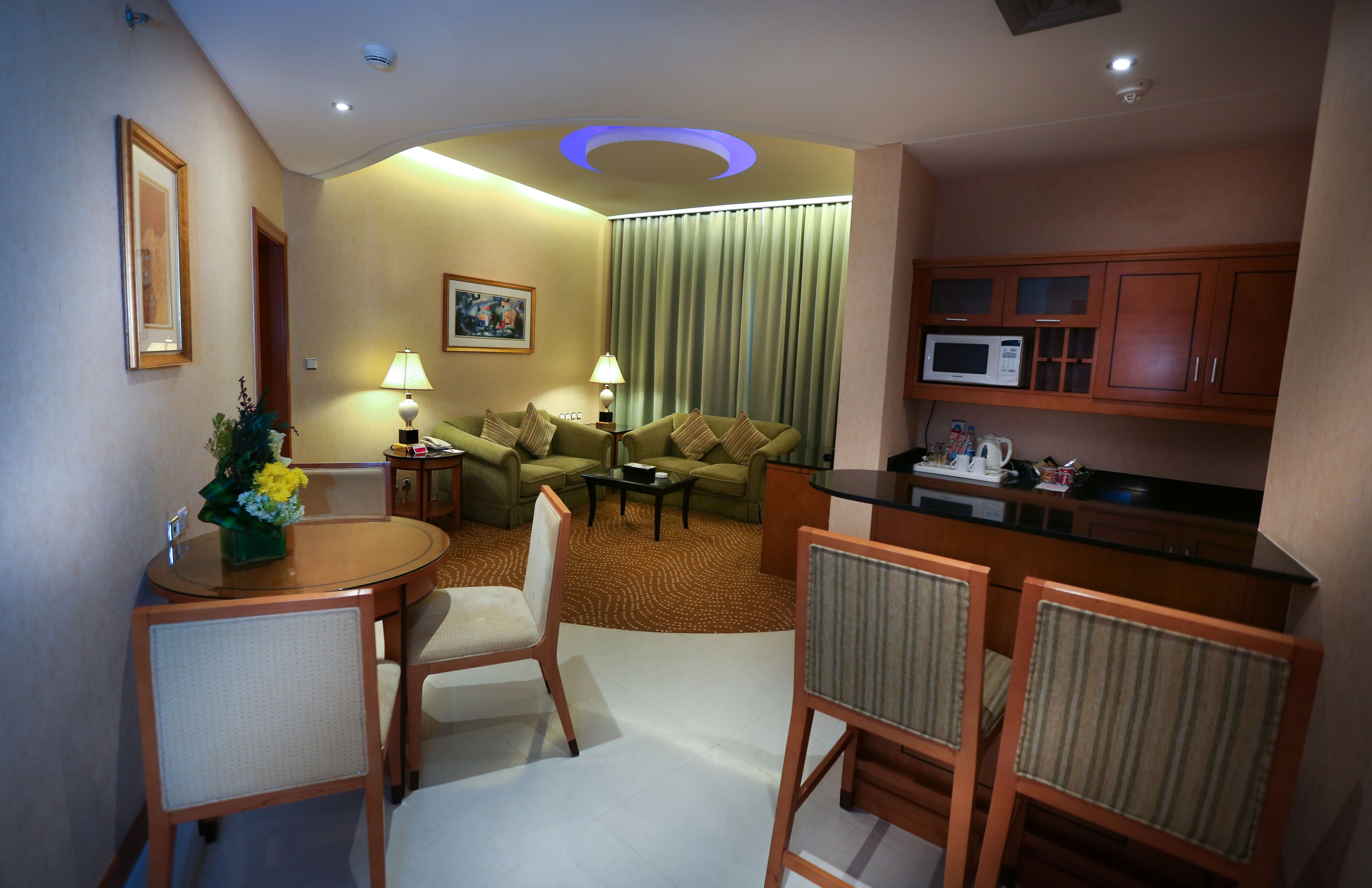 A compact hotel room with a dining area, a sofa, a small table with chairs, a microwave, and a television.