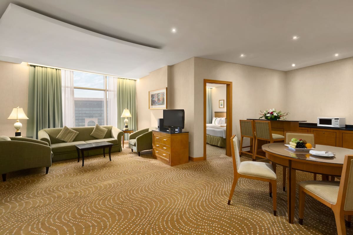 Habitación de hotel con sofá, mesa de centro, televisor, mesa de comedor con sillas, microondas y pequeña cocina.