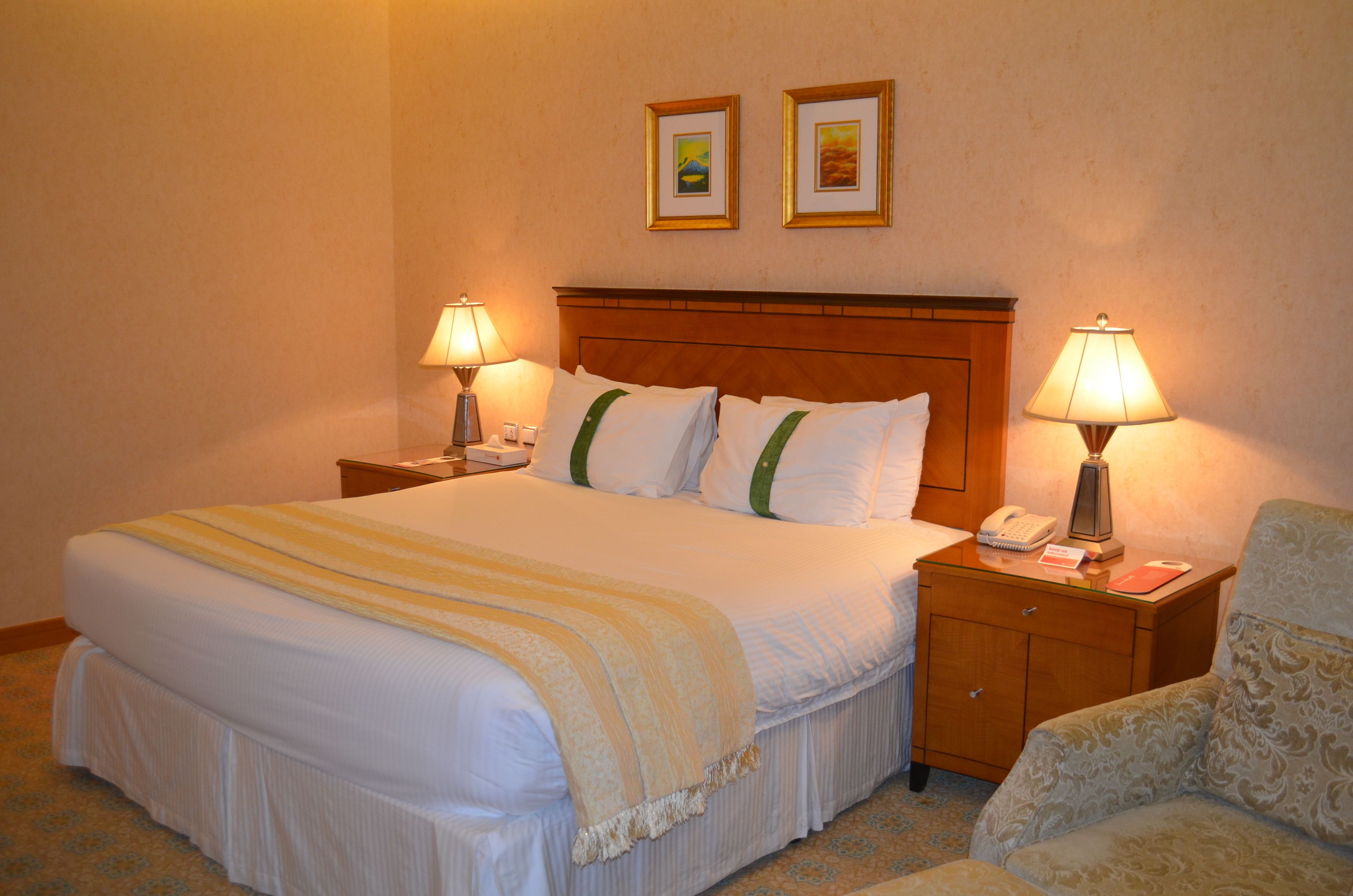 A hotel room with a large bed, two bedside lamps, a nightstand with a phone, and a chair.