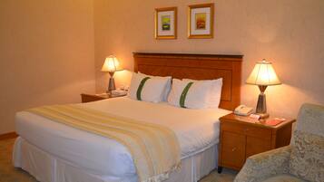 A hotel room with a large bed, two bedside lamps, a nightstand with a phone, and a chair.