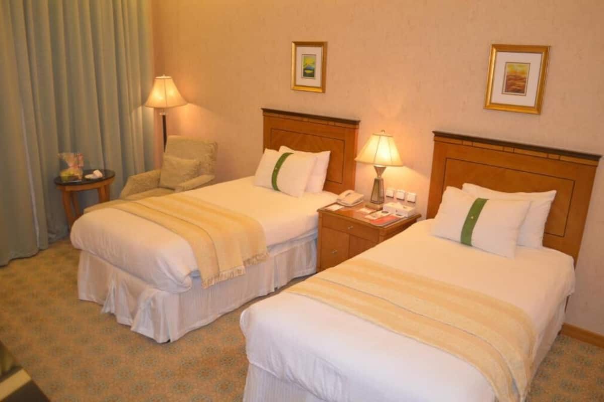 Una habitación de hotel con dos camas, una mesita de noche, una lámpara y una silla.
