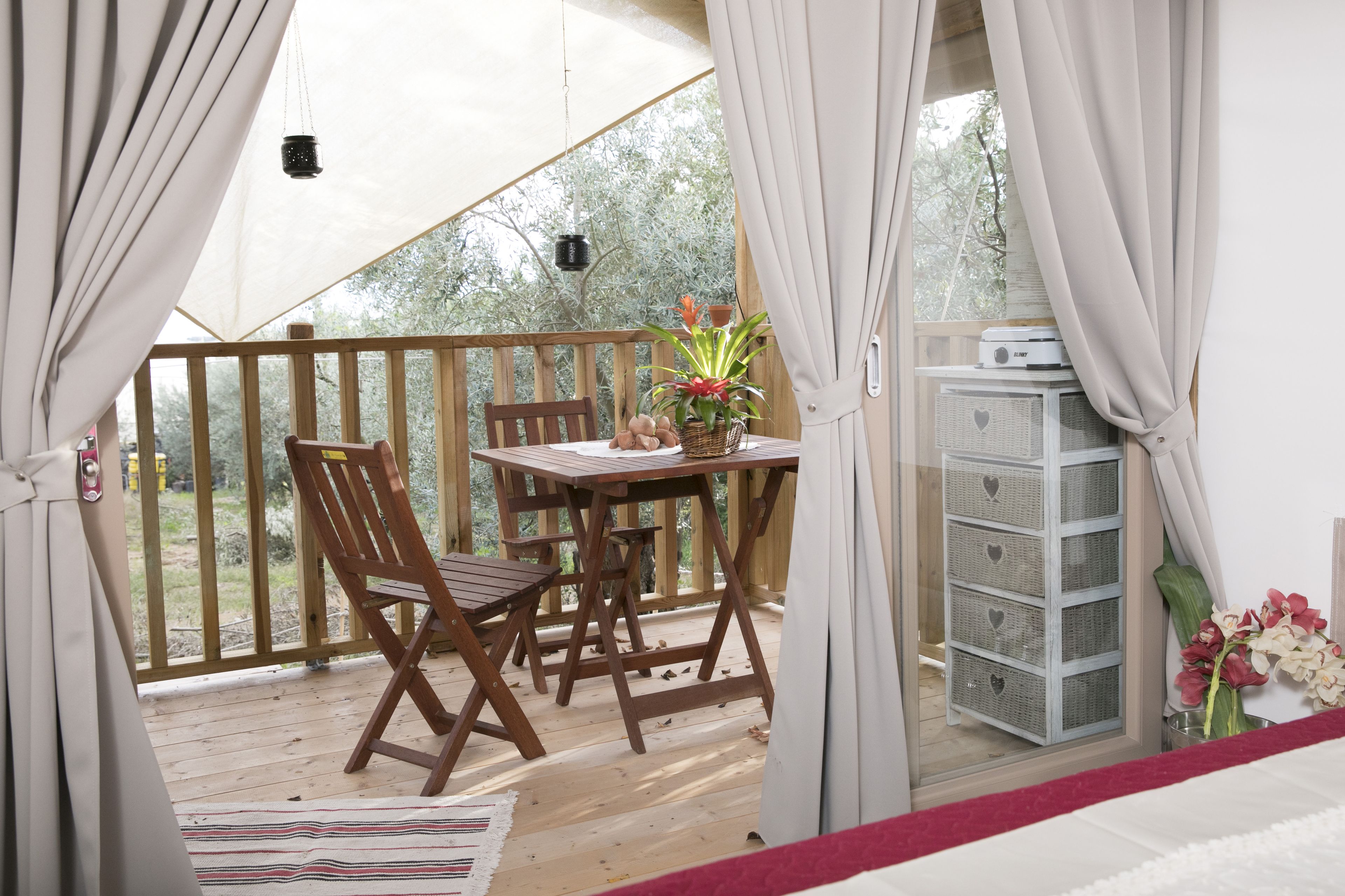 A wooden deck with a table and chairs, a hanging light fixture, and a small cabinet with a heart-shaped design.