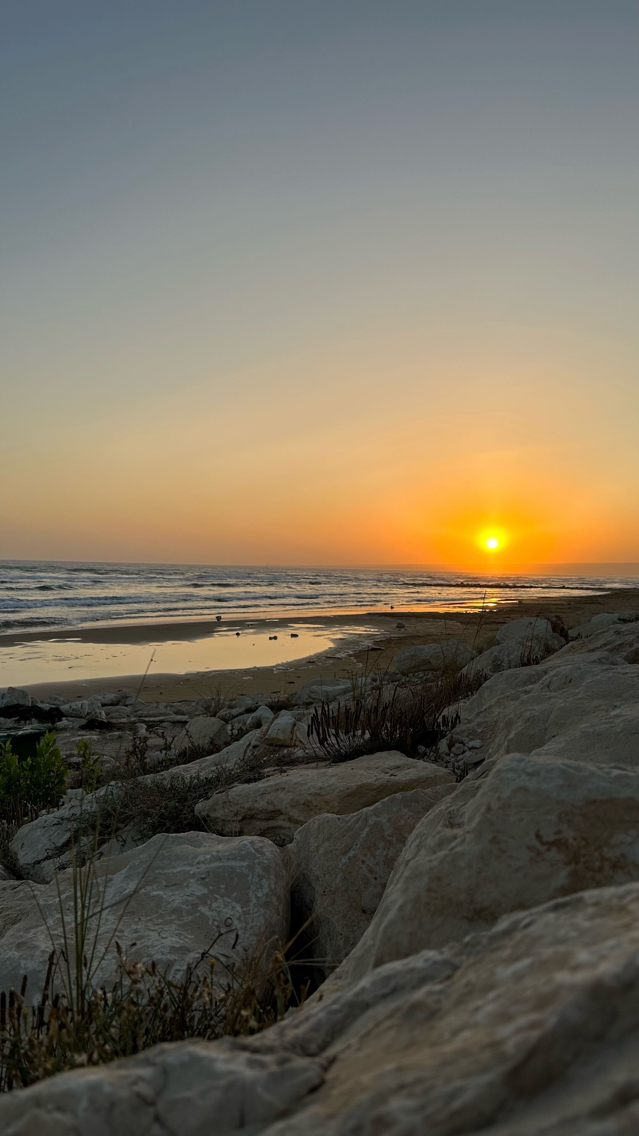 A rocky shoreline with waves and a sunset in the background.