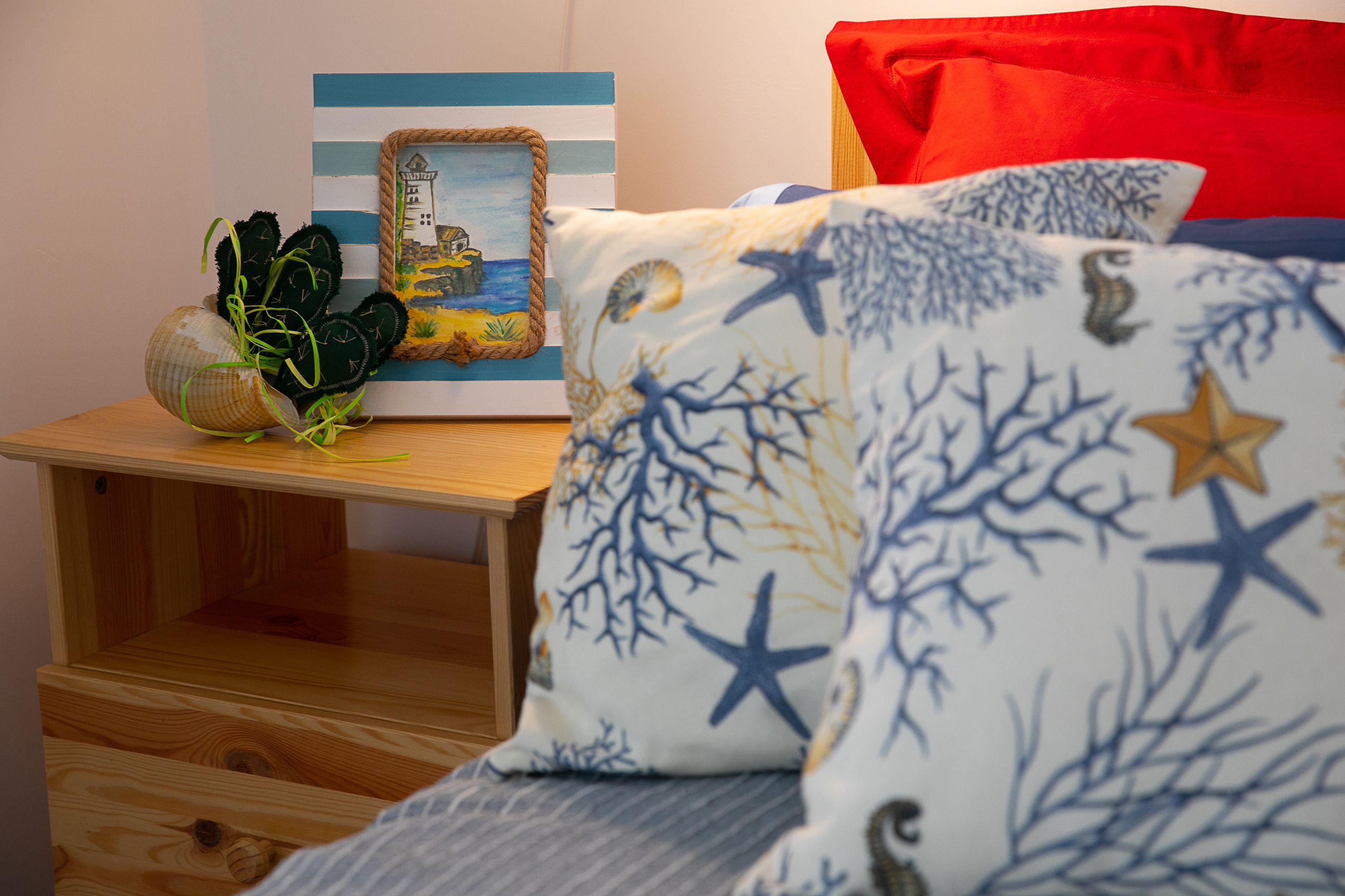 Ein ordentlich eingerichtetes Schlafzimmer mit einem Holznachttisch, einem gerahmten Bild und einem Bett mit einem blau-weißen Sternenmuster-Kissen.