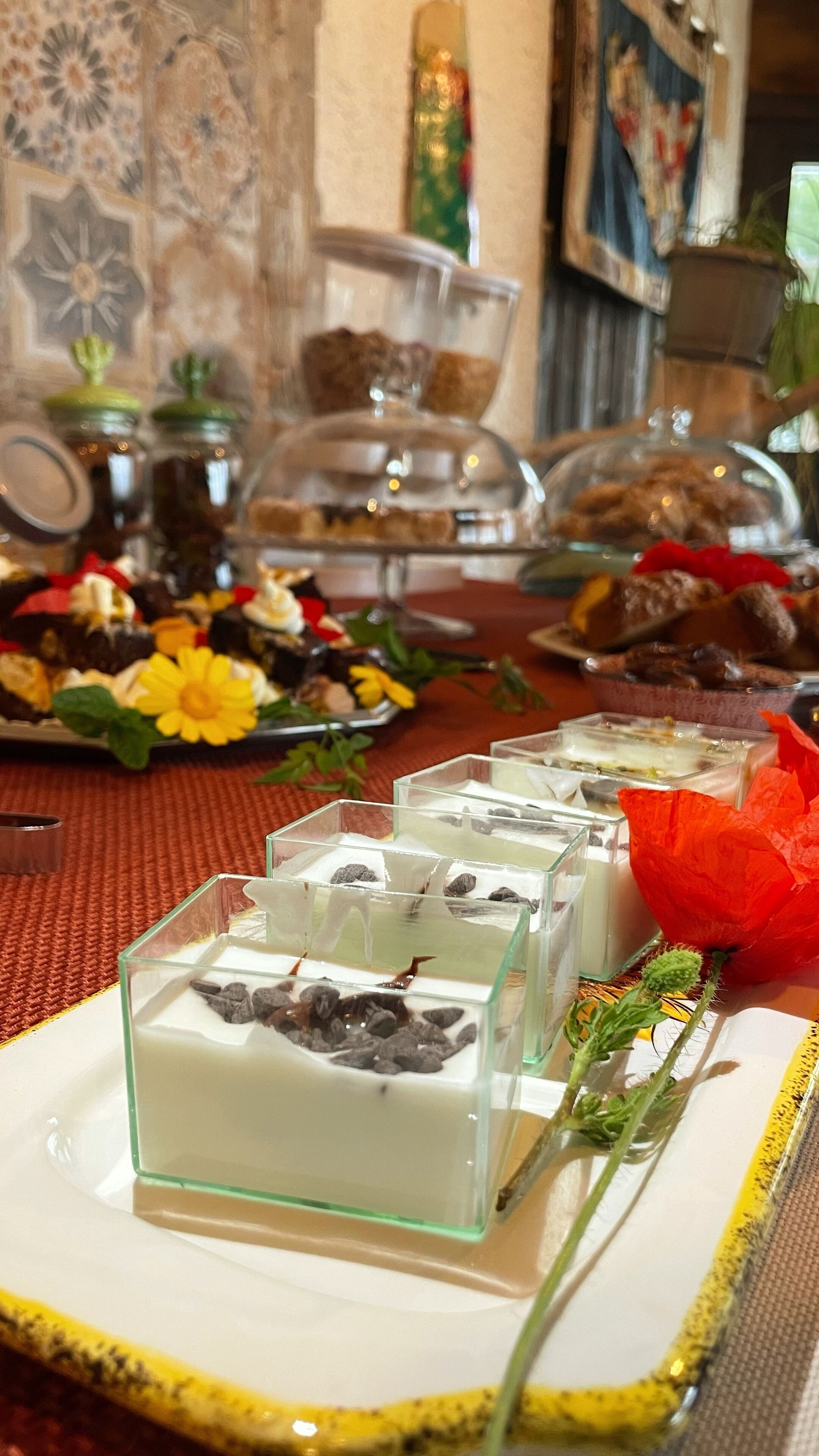 A table with various food items, including desserts in glass containers and a flower arrangement.