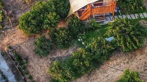 Vista aérea de una cabaña rústica con techo inclinado, rodeada de vegetación densa y un sendero de tierra que conduce a ella.