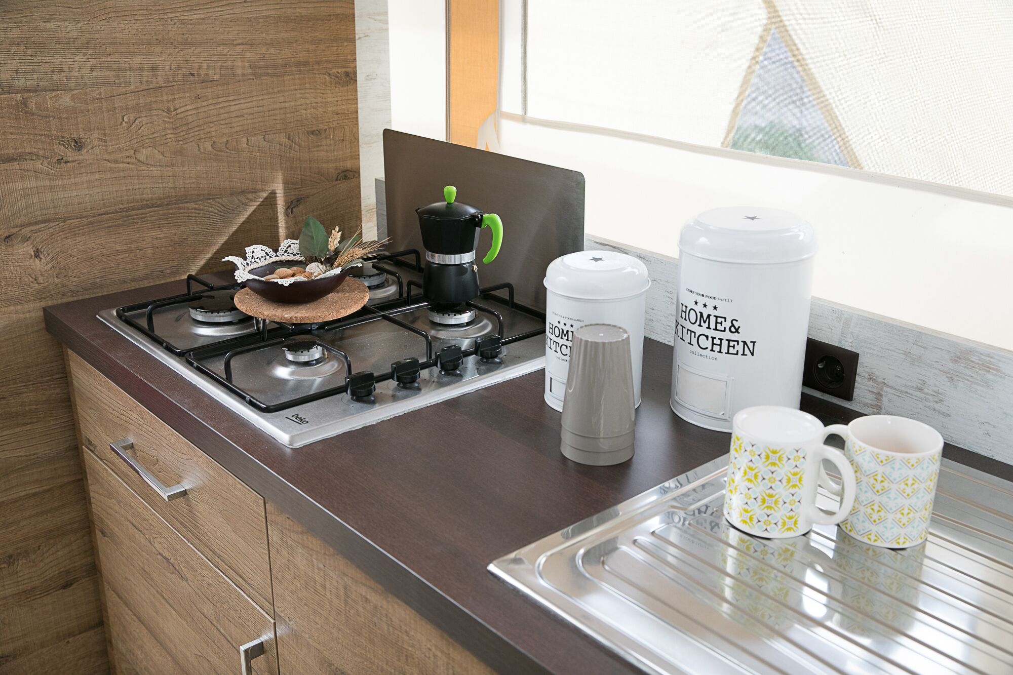 A kitchen with a gas stove, a coffee maker, a water dispenser, and two mugs on the counter.