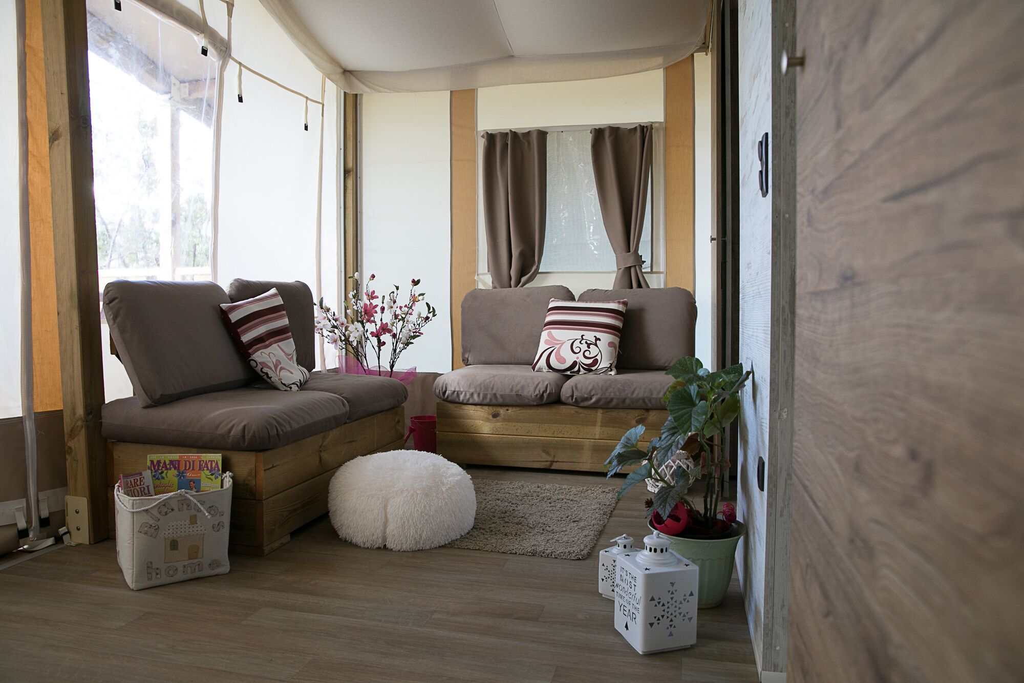 A cozy living area with a sofa set, a small round ottoman, a wooden floor, and a potted plant.