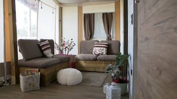 A cozy living area with a sofa set, a small round ottoman, a wooden floor, and a potted plant.