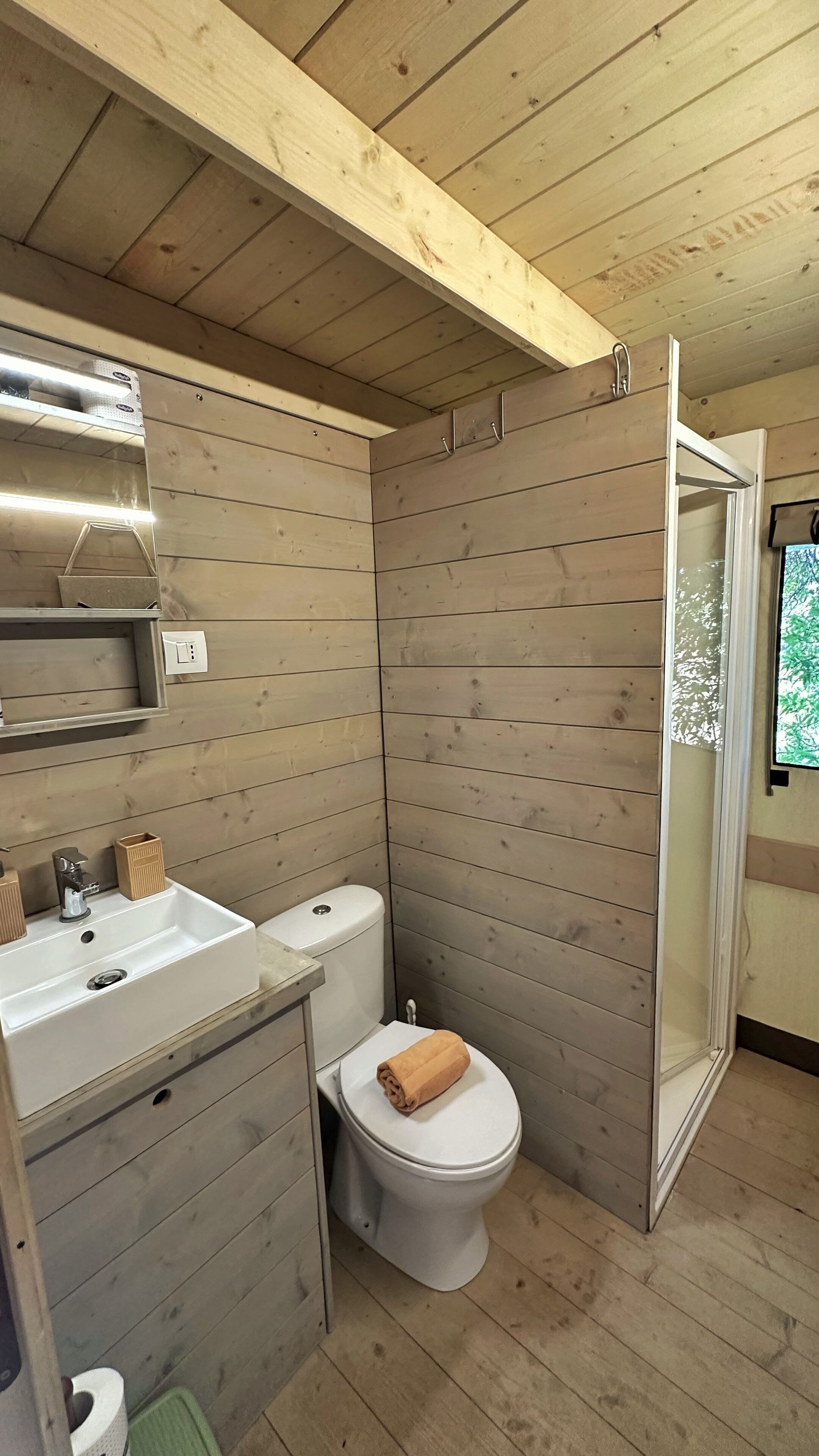 Un baño de madera pequeño y funcional con inodoro, lavabo y ducha.