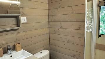 Un baño de madera pequeño y funcional con inodoro, lavabo y ducha.