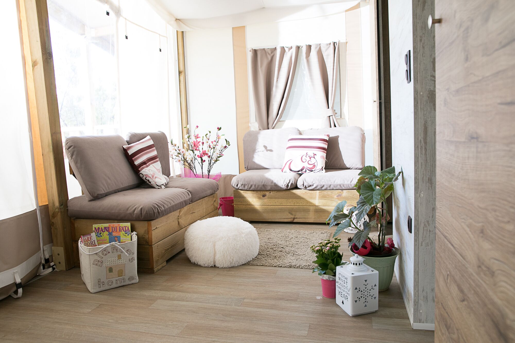 Un espacio de sala cómodo con un sofá, un banco de madera, un taburete blanco y una pequeña mesa con una planta.