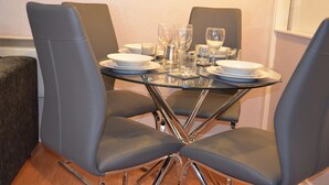 A dining table with four grey chairs, clear glassware, and white plates. - 28 Scotfield (Luton)