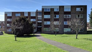 A multi-story residential building with a brick facade, a central entrance, and a small parking area. - 28 Scotfield (Luton)