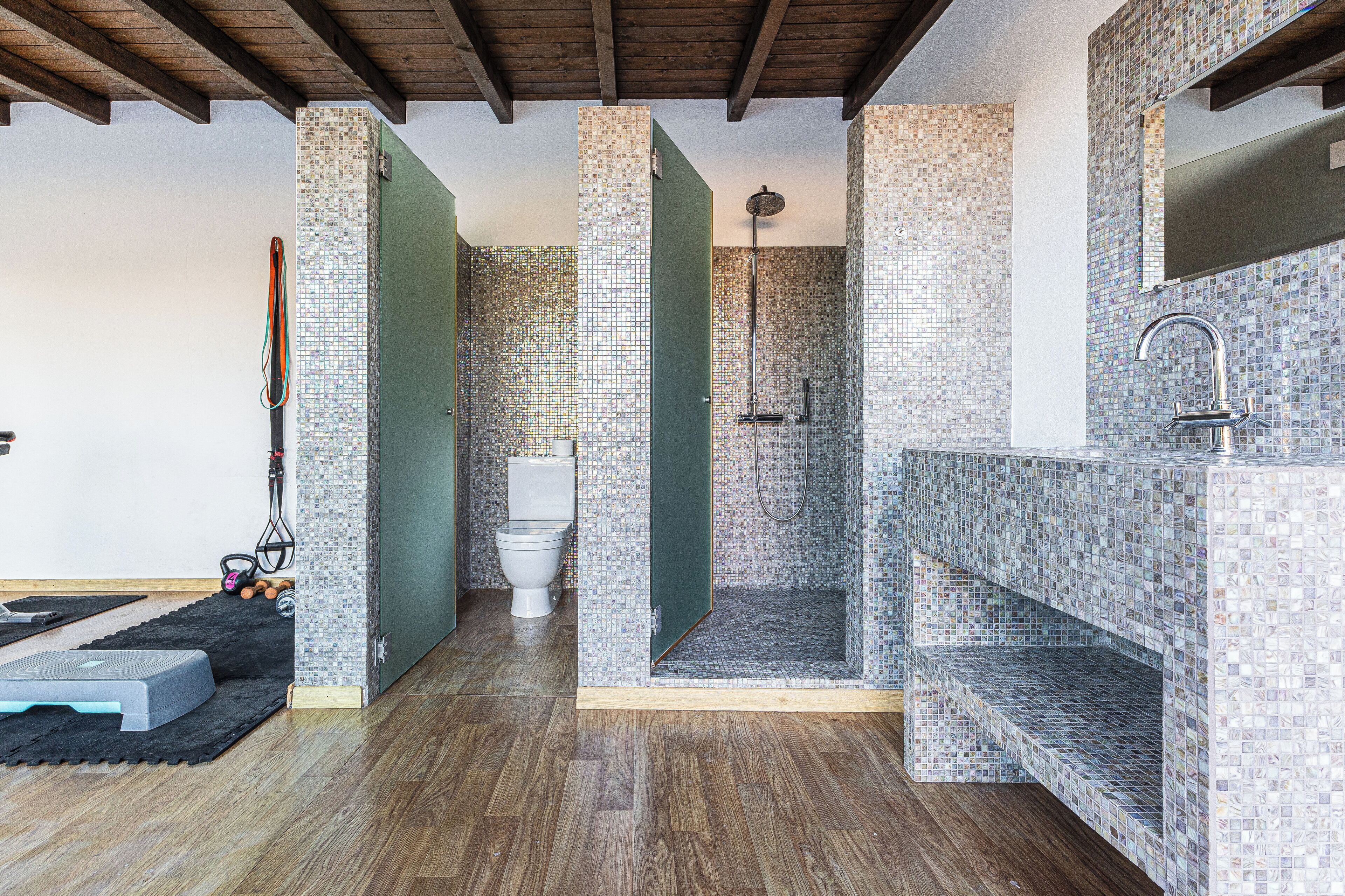 Une salle de bain équipée d’une douche, de toilettes et d’un lavabo, avec des murs recouverts de mosaïques et un plancher en bois.