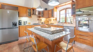 Een moderne keuken met houten kastjes, granieten werkbladen, roestvrijstalen apparatuur en hanglampen.