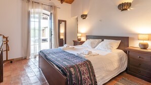 Een goed verlichte slaapkamer met een groot bed, een houten hoofdbord, een nachtkastje met een lamp en een spiegel aan de muur.