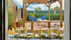 Een buiten-eetgedeelte met een houten pergola, een hangmat en uitzicht op het landschap.