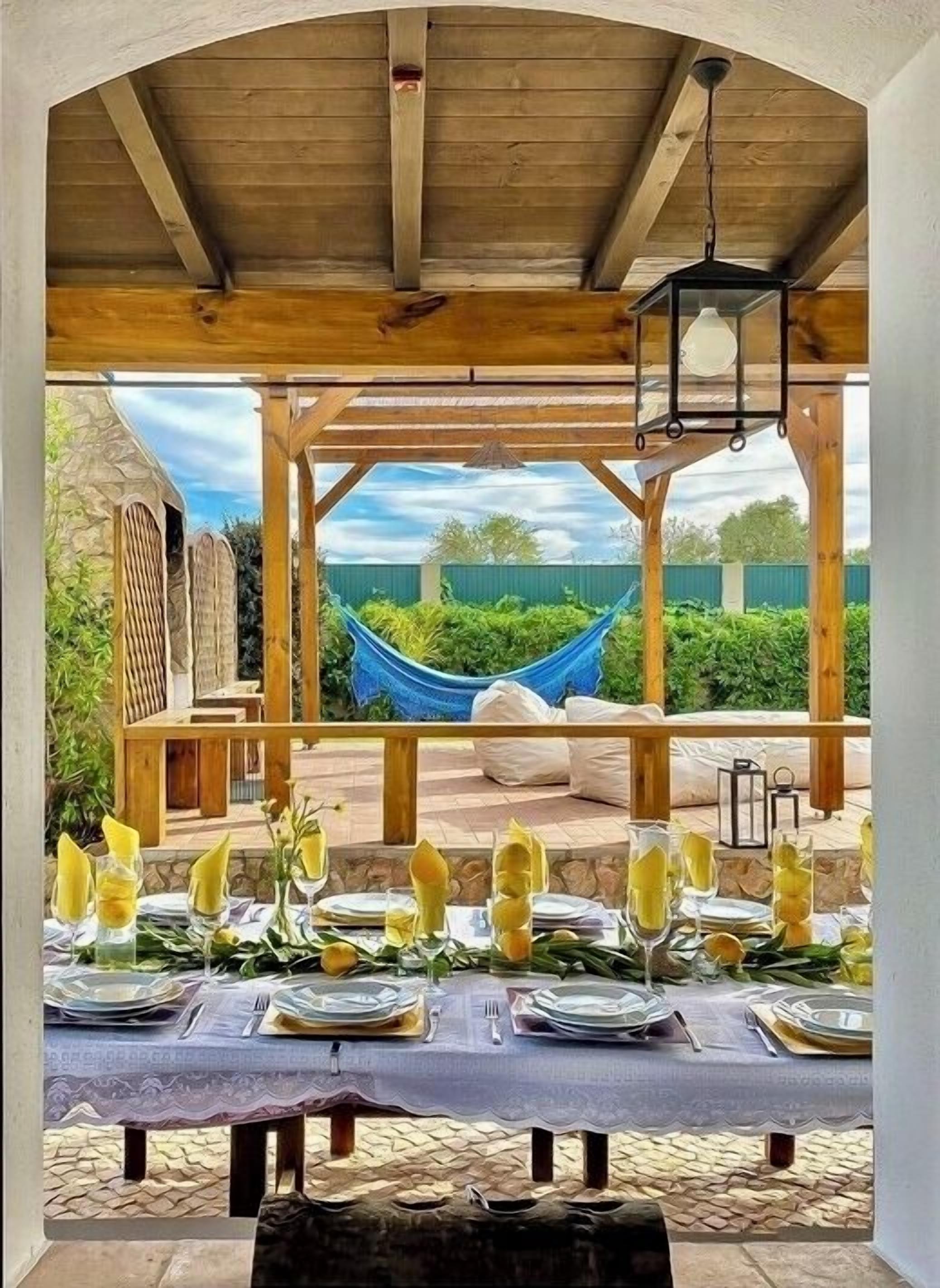 An outdoor dining area with a pergola, a hammock, and a view of greenery.