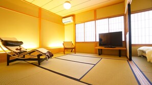 Une pièce de style japonais traditionnel, avec un sol recouvert de tatamis, une télévision, un canapé et un futon servant de lit.